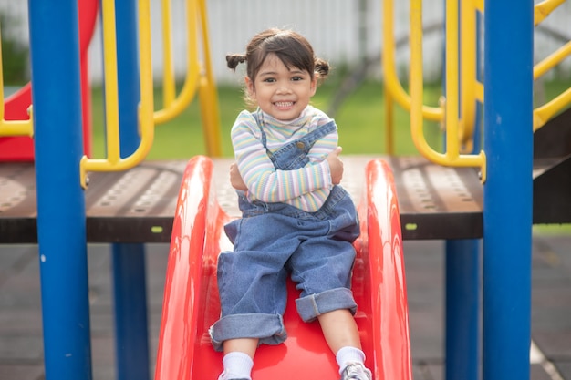 Asian Child girl playing on the outdoor playground. Kids play in school or kindergarten yard. Healthy summer activity for children.