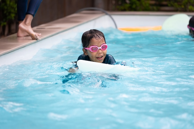 Asian child girl playing water and swimming in the swimming pool with her friend with fun. Summer activity and childhood lifestyle concept.