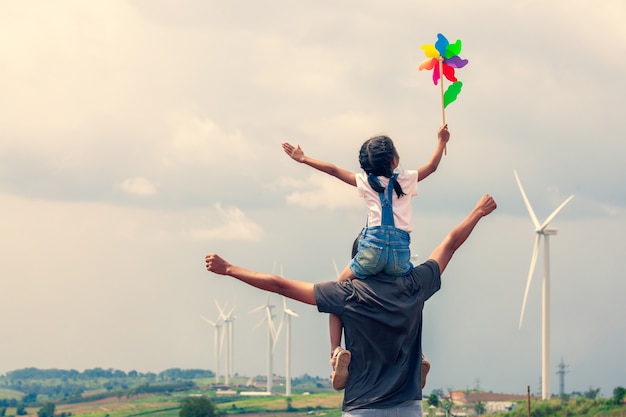 Asian child girl playing with wind turbine and riding on father's shoulders