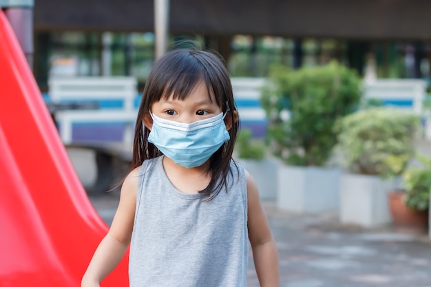 Asian child girl smiling and wearing fabric mask She playing with slider bar toy at the playground