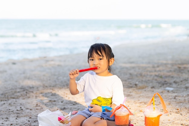 Asian child happy girl eating a food on the beach At the sea Summer season