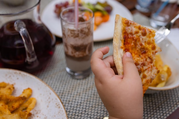 Asian child holding slice of delicious hot pizza over table