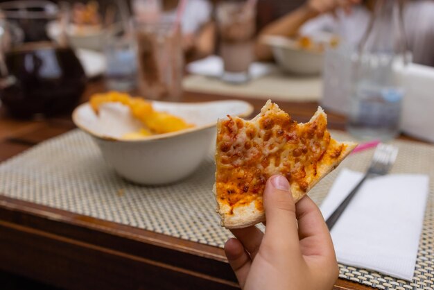 Asian child holding slice of delicious hot pizza over table