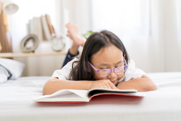 Asian child little girl reading books lying on the bed at home