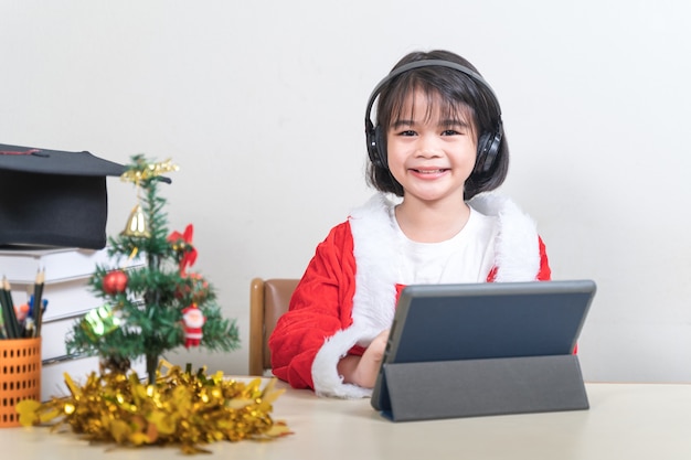 Asian children little girl dress Christmas Santa Claus chatting with friends on digital tablet. Christmas Holiday Concept Stock Photo