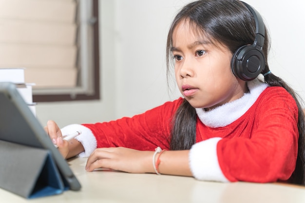 Asian children little girl dress Christmas Santa Claus chatting with friends on digital tablet. Christmas Holiday Concept Stock Photo