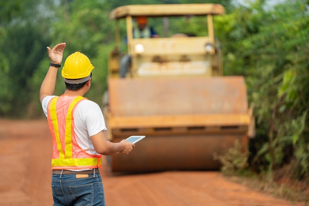 Asian civil engineer operate with tablet to control working soil compaction machine compacting soil under the road construction in the countryside