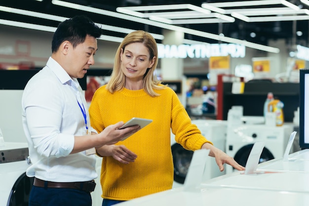 Asian consultant salesman in electronics and household appliances store selling a working machine to