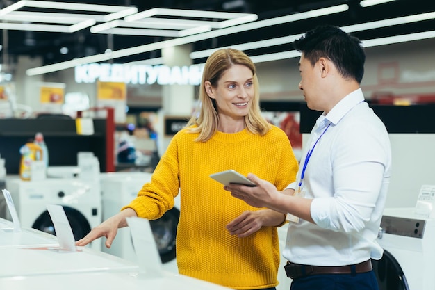 Asian consultant salesman in electronics and household appliances store selling a working machine to