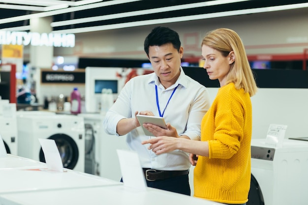 Asian consultant salesman in electronics and household appliances store selling a working machine to