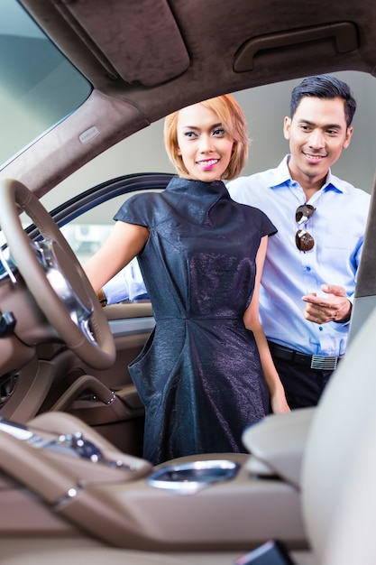 Asian couple choosing luxury car in auto dealership looking at the interior