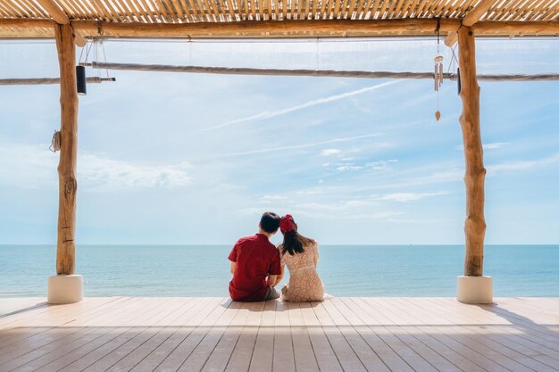 Asian couple relaxing on wooden terrace in tropical sea on summer vacation