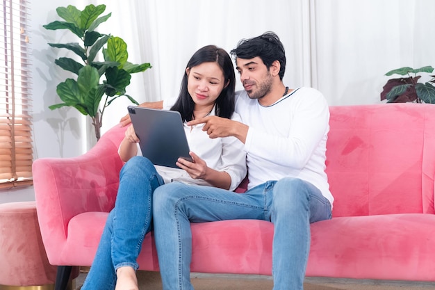 Asian couple sitting on couch with tablet pc celebrating online win great deal or business success at home free space Millennial spouses enjoying big sale in web store