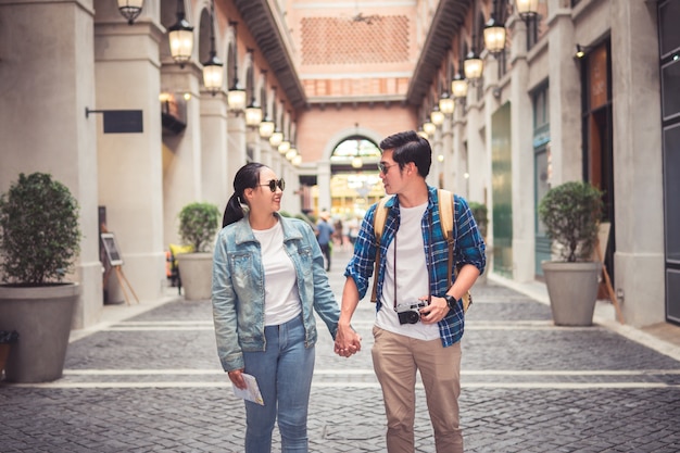 Asian couple tourist backpackers walking in street while traveling on holidays with camera and paper