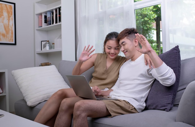 Asian couple using laptop to connect with family for video call Man and Woman using laptop computer in living room at home