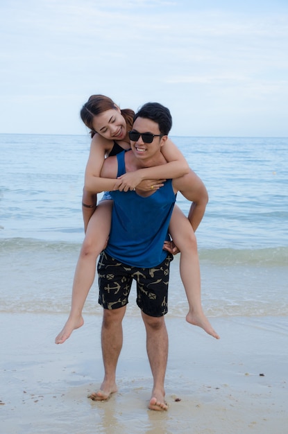 Asian couple walking on beach, with girl ride on one's back