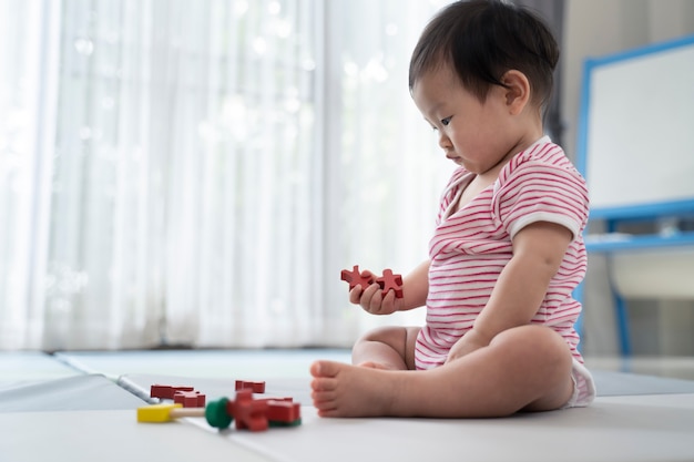 Asian cute baby sitting and playing a small toy on soft mat at home.