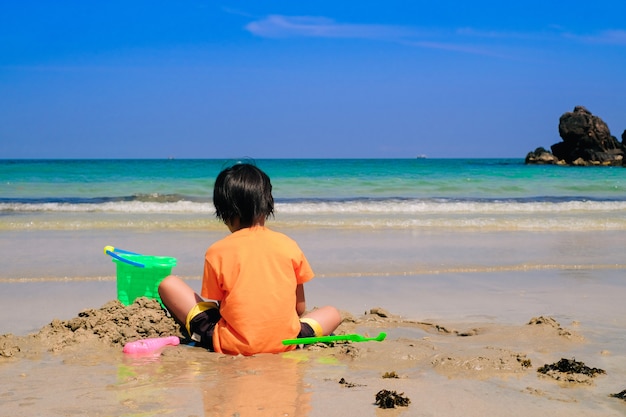 Asian cute boy playing the sand alone on the beach.