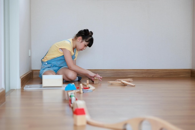 Asian cute girl playing wood block building rail way and road on the floor at home