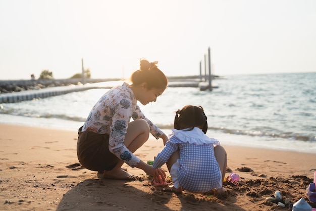 Asian cute little girl and her mother playing or making sand castle or digging with sand on tropical beach Children with beautiful sea sand blue sky Happy kids on vacations seaside on the beach