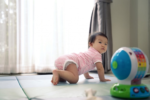 Asian cute scamp baby crawling on soft mat at home and turning look back to see what happen.