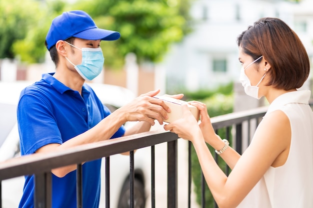 Asian deliver man in blue shirt handling package and give to young woman costumer at house.