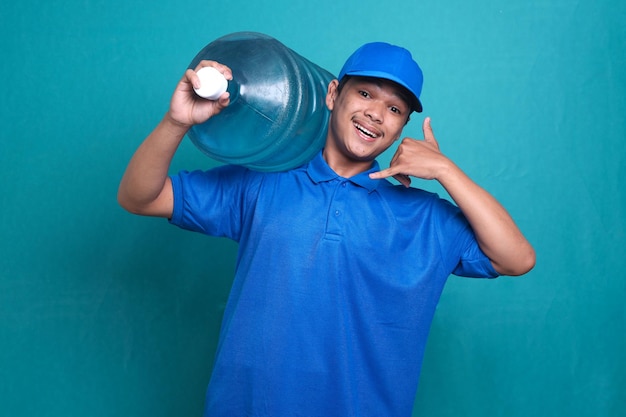 Asian delivery guy in blue uniform work as dealer courier, holding water bottle while doing phone ge