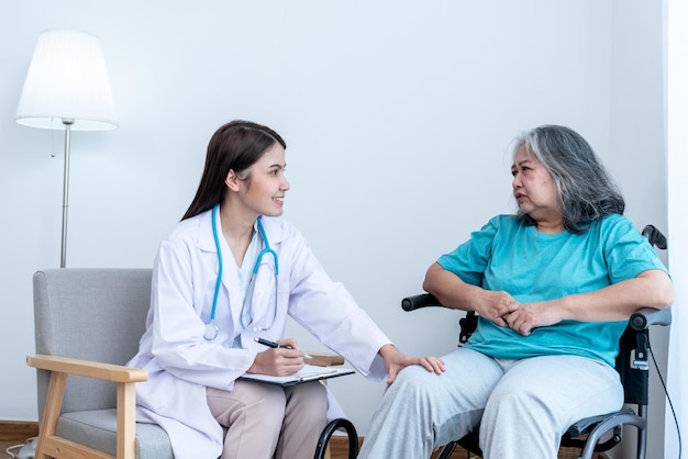 Asian doctor asking about illness and encourage elderly woman patient who is sitting in a wheelchair