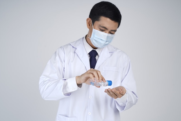 Asian doctor man wearing white coat, medical mask and holdinging sanitizer