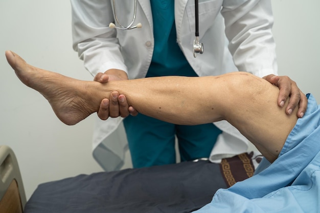 Asian doctor physiotherapist examining massaging and treatment knee and leg of senior patient in orthopedist medical clinic nurse hospital