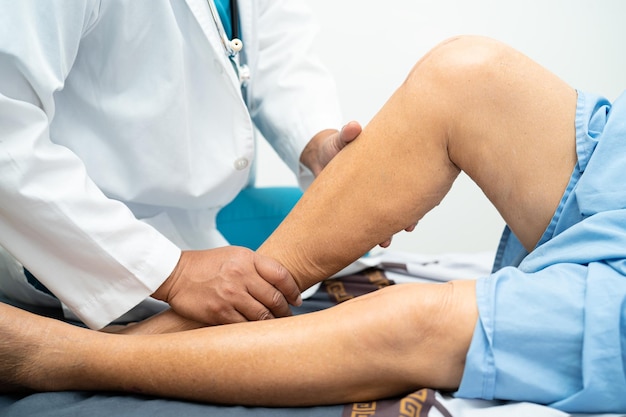 Asian doctor physiotherapist examining massaging and treatment knee and leg of senior patient in orthopedist medical clinic nurse hospital