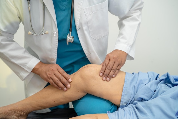 Asian doctor physiotherapist examining massaging and treatment knee and leg of senior patient in orthopedist medical clinic nurse hospital