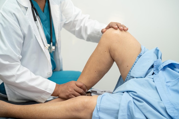 Asian doctor physiotherapist examining massaging and treatment knee and leg of senior patient in orthopedist medical clinic nurse hospital