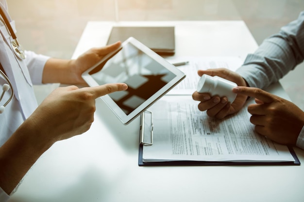 Asian doctor talking the patient at clinic while using the tablet explaining the patient condition and the treatment result