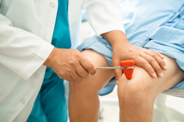 Asian doctor use hammer knock senior woman patient to check knee reflex nerve and muscle in hospital