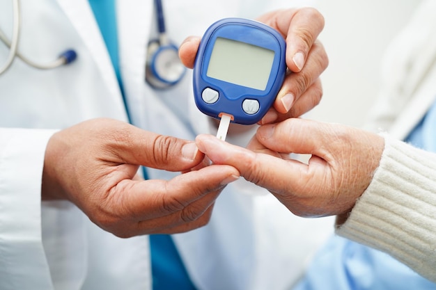 Photo asian doctor using digital glucose meter for check sample blood sugar level to treatment diabetes