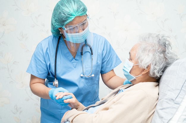 Asian doctor wearing face shield and PPE suit to check patient