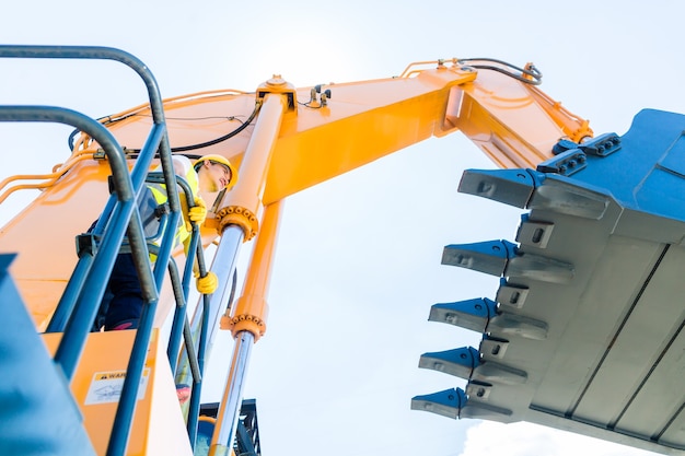 Asian driver standing on construction machinery on building site