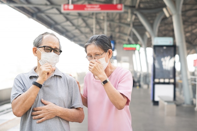 Asian elder senior couple wearing mask for prevent Covid-19 or Coronavirus infection at train station.