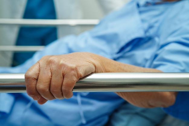 Asian elder senior woman patient holding bed rail while lie down with hope waiting her family in hospital