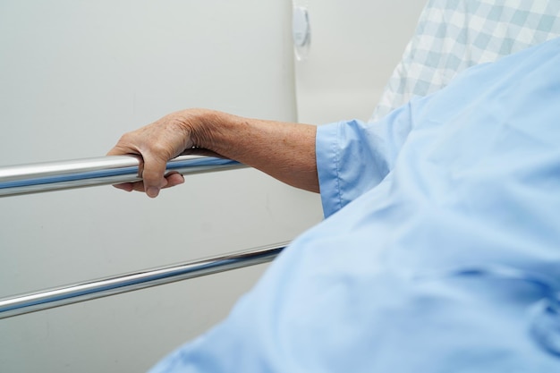 Asian elder senior woman patient holding bed rail while lie down with hope waiting her family in hospital