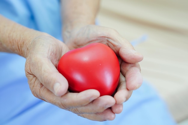 Asian elder senior woman patient holding red heart in hospital