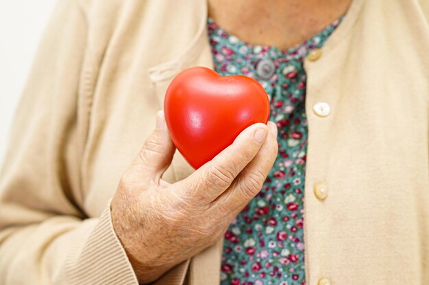 Asian elder senior woman patient holding red heart in hospital