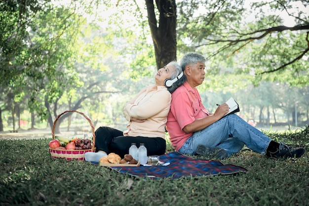 Asian elderly couple attractive wife and husband picnic and relaxing on the green lawn in garden