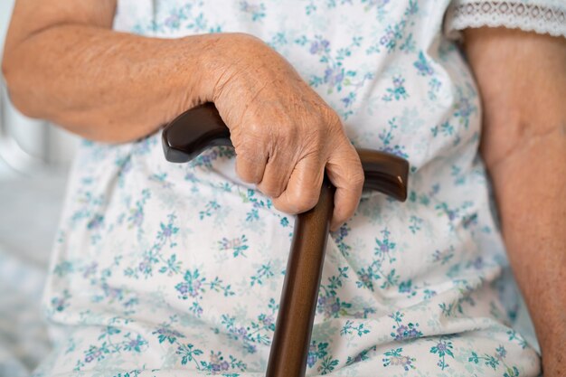 Asian elderly disability woman holding waling stick wood cane round handle walking aid for help to walk