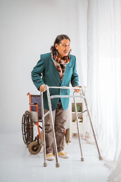 Asian elderly man smiling standing in front of wheelchair trying to walk with walker frame happily