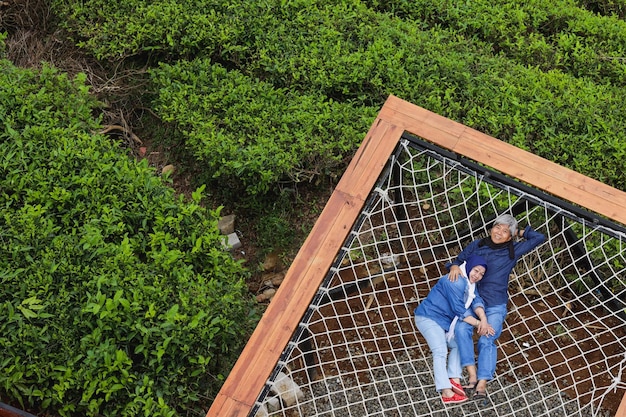 Asian elderly romantic couple lying on aesthetic net at tea plantation Happy and healthy spouse