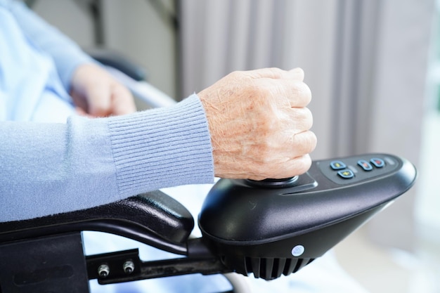 Asian elderly woman disability patient sitting on electric wheelchair in park medical concept