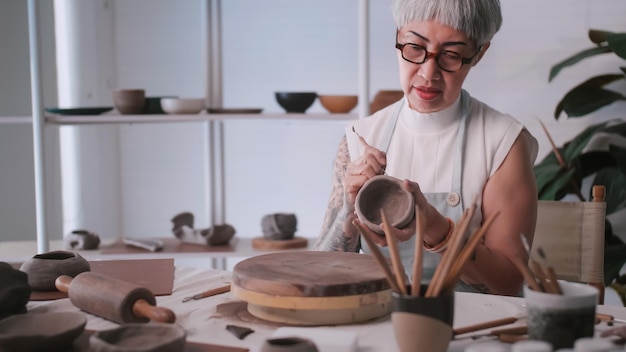 Asian elderly woman enjoying pottery work at home A female ceramicist is making new pottery in a studio