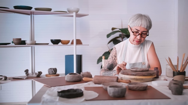 Asian elderly woman enjoying pottery work at home A female ceramicist is making new pottery in a studio